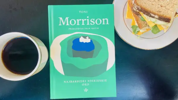 Zielona okładka książki Toni Morrison "Najbardziej niebieskie oko" leży obok filiżanki kawy i kanapki.