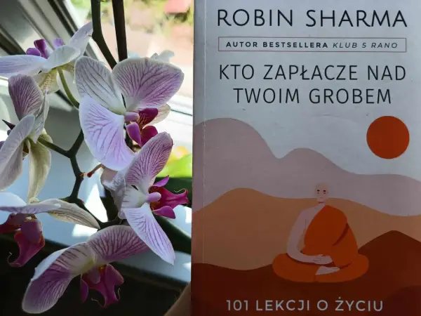 Delikatne storczyki obok książki "Kto zapłacze nad twoim grobem" Robina Sharmy, autora bestsellerów.